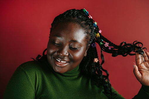 Beautiful African woman with braided hair and colorful clips smiling on red background