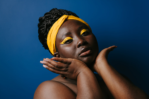 Portrait of confident African woman with beautiful make-up and jewelry touching face on blue background