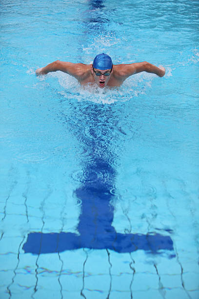 Swimmer with blue cap performing butterfly stroke in pool stock photo