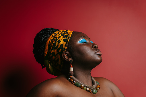 Beautiful plus size African woman with colorful make-up wearing traditional headwear on red background