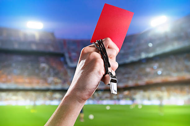 Referee Holding Up A Red Card And Whistle Inside A Stadium Stock