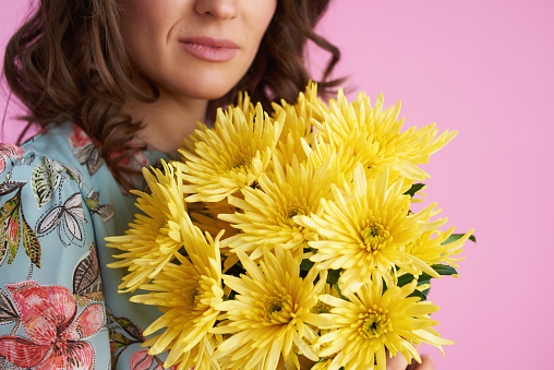 Closeup on woman with yellow chrysanthemums flowers against pink background.