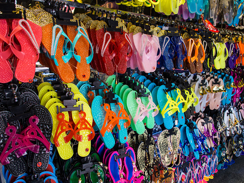 In the dim hum of a Bangkok market, flip-flops dangle like tropical fruit. Their rainbow hues whisper promises of beach days, waiting patiently for toes to claim their vibrant embrace.