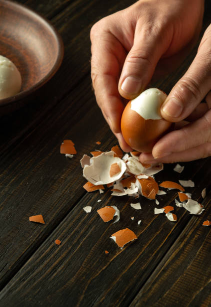 istock Close-up of a man hands peeling a boiled egg on a kitchen black table for a snack. Dark space for inscription. 1859801428