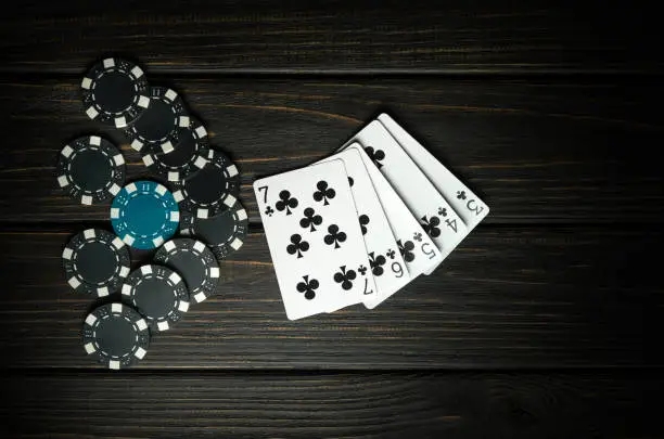 Photo of Popular poker game with straight flush winning combination. Cards with chips on a black vintage table in a poker club. Free black space for ads