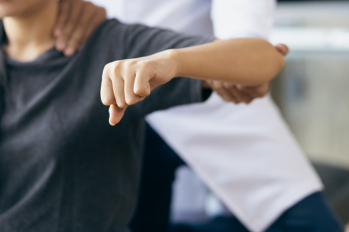 Doctor practicing arm and shoulder physiotherapy for female patient in hospital.