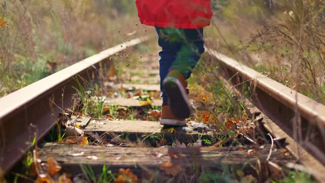 A boy walking on old railroad in the forest in autumn time