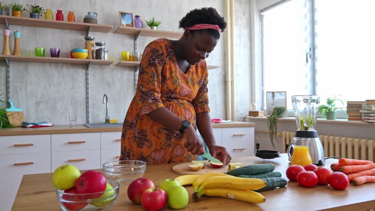 Pregnant Black Woman Cutting Apples For A Healthy Fruit And Vegetable Smoothie At Home