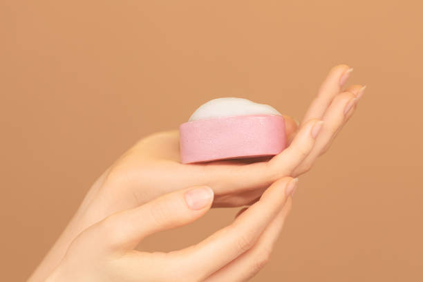 istock Close-up of female hands palm with pink solid face cleanser on peach background. 1859831670