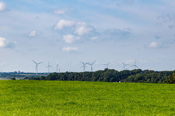 istock Green plain with leafy trees and windmills in background against misty blue sky 1859832221