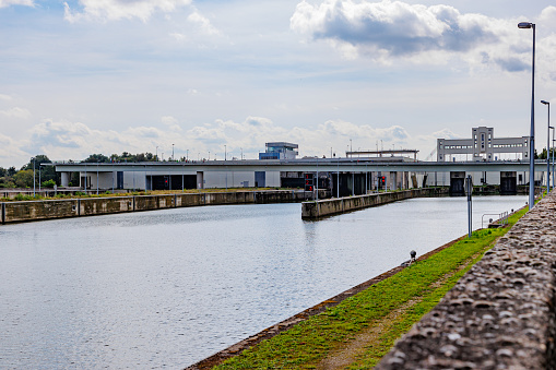 Canal towards Lanaye lock complex with closed floodgates, Albert canal, construction walls, vehicular bridge in background against misty sky, sunny summer day in Ternaaien, Belgium