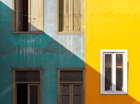 Artistic and abstract composition of a yellow and grey facade in Lima, Peru. Windows, oblique and diagonal shadow.