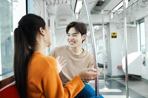 Couple of diverse young friends standing and talking together on sky train. Multiracial people having fun while commuting by a train. Public transport, people concept.
