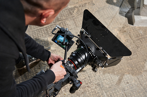 a professional cameraman holds a video camera from the floor level and shoots a lower angle. looking at camera monitor