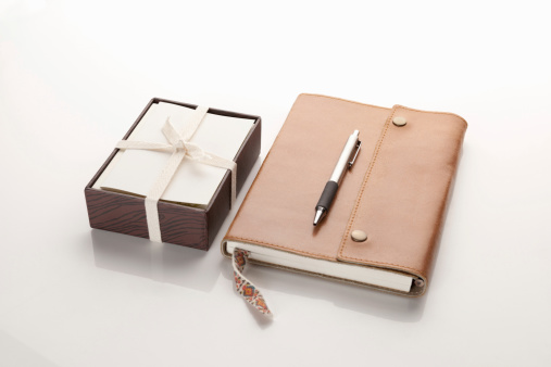 Leather notebook and pen by box of notecards tied with a bow on white background