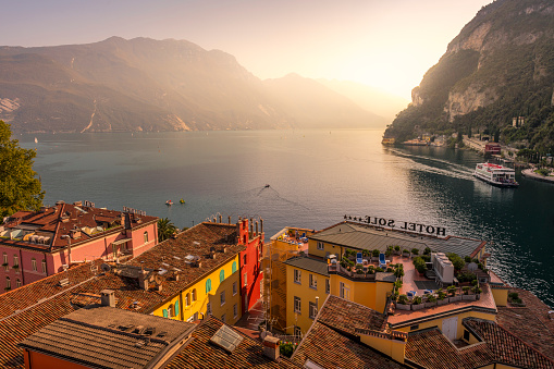 Riva del Garda, Italy - October, 1. 2023:  Sunrise at Lake Garda in Riva del Garda. In front are some rooftops from hotels.