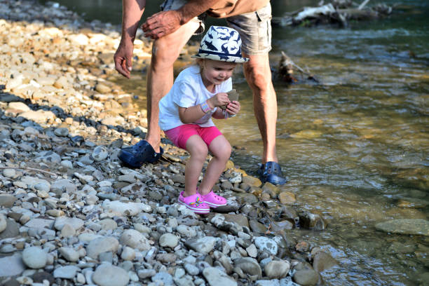 A little girl picks up and throws a stone from the ground and throws it into the river stock photo