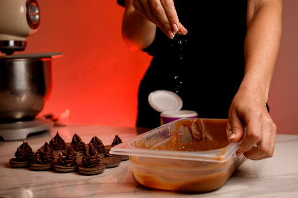 las manos femeninas de los pasteleros espolvorean crema de chocolate en un recipiente de plástico con virutas de coco - almond macaroon fotografías e imágenes de stock