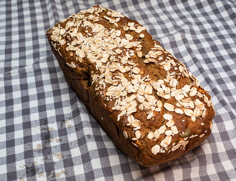 Freshly baked oat bread, a wholesome delight, resting on a linen cloth adorned with hues of white, blue, and grey, presenting a rustic and inviting image.