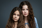 Studio portrait of two beautiful sisters in blue shirts and jeans against gray background