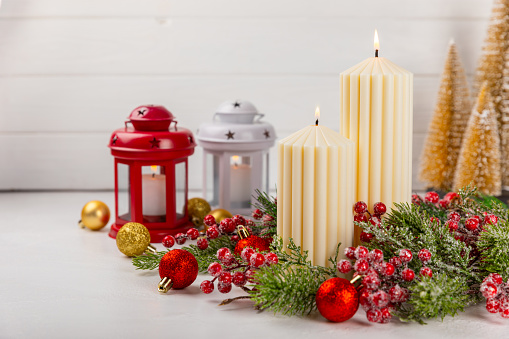 Christmas backgrounds: three red burning Christmas candles shot on rustic wooden table. The composition is at the left of an horizontal frame leaving useful copy space for text and/or logo at the right.\nString light and Christmas decoration are out of focus at background. Predominant colors are red and brown. High resolution 42Mp studio digital capture taken with Sony A7rII and Sony FE 90mm f2.8 macro G OSS lens