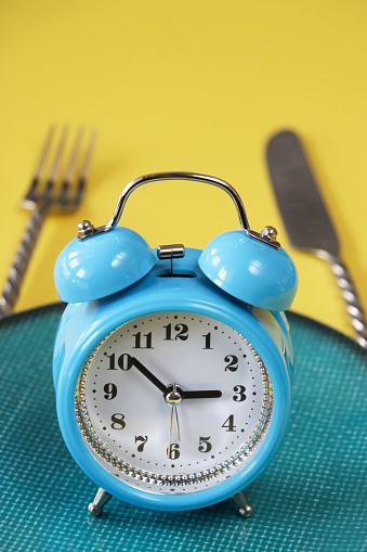 Stock photo showing close-up view of a healthy eating and intermittent fasting diet concept depicted by a plate containing a double bell alarm clock.