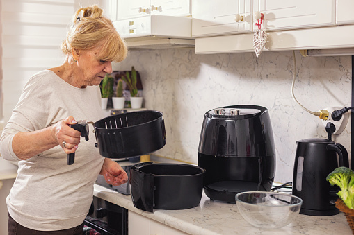 Senior woman using air fryer to prepare healthy vegetarian meal
