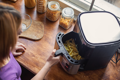 Beautiful teenage girl using an air fryer in the kitchen to prepare french fries