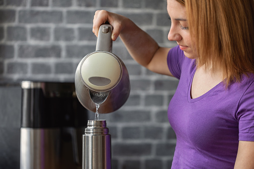 Beautiful teenage girl using electric kettle to to make tea