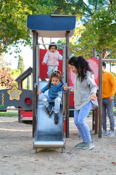 Dominican mother playing with her children at the slide in a park. stock photo