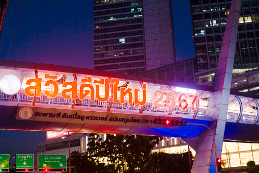 Illuminated thai letters for Happy New Year 2024 at modern footbridge. Illuminated modern footbridge is at Ratchada 23 in Bangkok over junction of Ratchadaphisek Rd and Thiam Ruam Mit Rd.