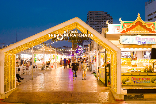 Gate and restaurants and market stalls of night market One Ratchada which is new night market on area of former Esplanade night market near Ratchadaphisek Rd. Night market is behind Esplanade mall at Ratchadaphisek Rd in southern Huai Khwang. Some people and tourists are walking in scene and aisle between market stalls