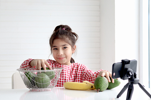 Happy girl record social media channel blogger vlog on digital smartphone cam. Little kid blogger influencer talking about fruits healthy food diet, streaming online podcast on mobile phon