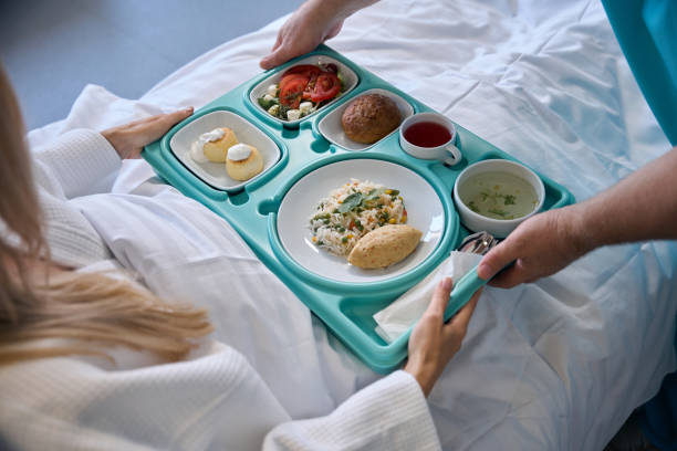 istock Nursing assistant serving meal to recumbent patient 1860103459