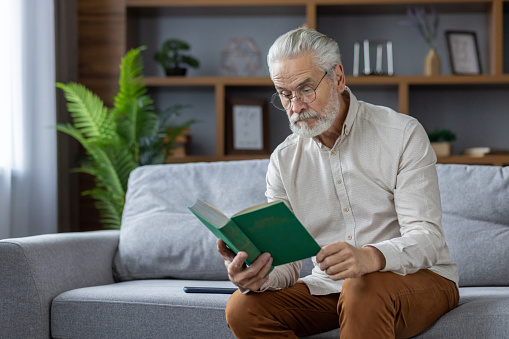 Senior man looking at the childhood photo album while sitting on the couch at home.