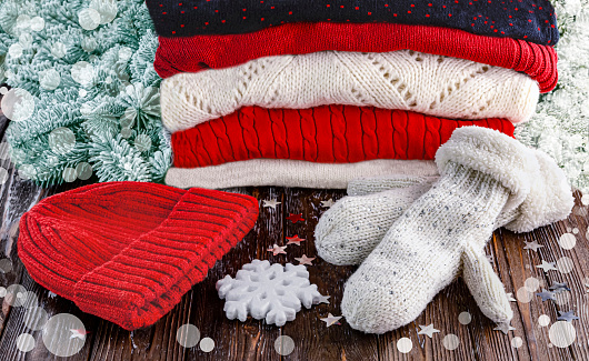 Stack of red and white winter woolen sweaters, red hat, woolen mittens on wooden background with Christmas decoration. Winter clothes concept