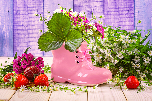 Pink boot and bouquet of summer wildflowers, ripe red strawberries on the table. Hello summer concept