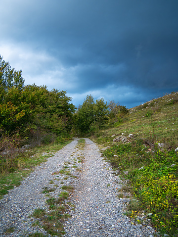 Unpaved road under dramatic storm clouds through the hilly landscape of the Croatian Coastal Mountains.