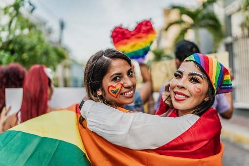 Portrait of a lesbian couple walking embraced with a rainbow flag in a social movement protesting outdoors