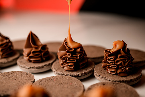 Close-up photo of halves of chocolate macaroons decorated with chocolate cream, decorated with another caramel cream