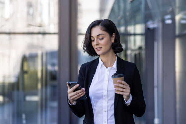 istock A young female office worker is standing outside an office center on a work break, holding a coffee and using the phone 1860200311