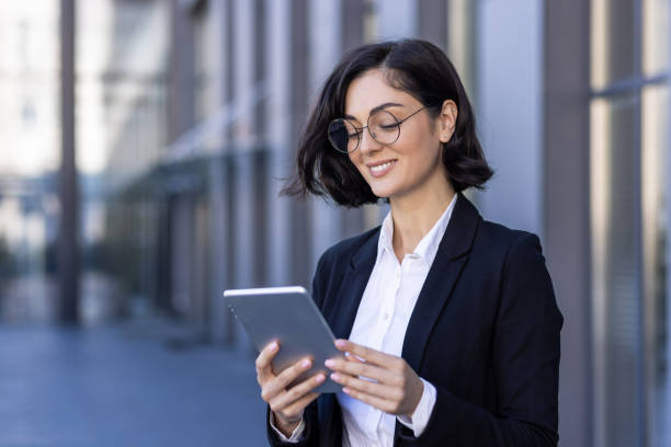 istock A smiling young businesswoman is standing near an office building and using a tablet. Talks on a video call, texts, close-up photos 1860200319