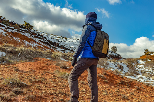 Burgos province, Castilla y León, Spain. Rear view of a cold-weather-clad hiker in a snowy mountain area with clayey ground