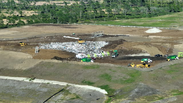 Aerial view of big landfill dumping site with bulldozer tractors burying large amount of trash under the ground. Harmful impact of modern consumerism on environment