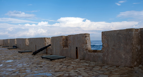 Firkas Fortress worn wall, antique cannon on paved yard at Old Town of Chania Crete, Greece. View of ripple sea from Revellino castle opening.