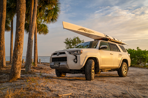 Skyway Beach, FL, USA - November 22, 2023: Toyota 4runner SUV with a rowing shell, LiteRace 1x by Liteboat on roof racks on a Florida beach.