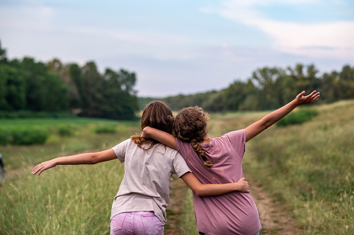 two teenage girls are enjoying the view of the meadow, hugging each other