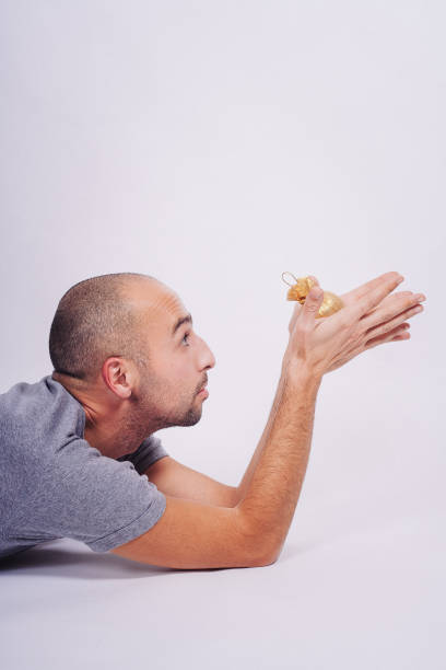 **MRs before late 2009 were allowed to have same MR of person for every shooting after signing it**  Middle-aged bald man, wearing a T-shirt, lying on front, holding Christmas ornaments and pondering, on white background