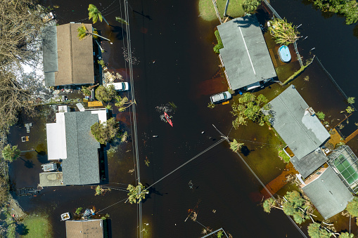 Consequences of natural disaster. Kayak boat floating on flooded street surrounded by hurricane Ian rainfall flood waters homes in Florida residential area.