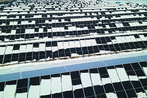 Aerial view of snow melting from covered solar photovoltaic panels at sustainable electric power plant for producing clean electrical energy. Low effectivity of renewable electricity in winter.